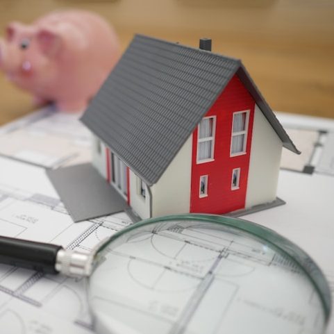 Gayrimenkul yatırımı ve konut değerlendirme: Mimari plan üzerinde ev maketi ve büyüteç.