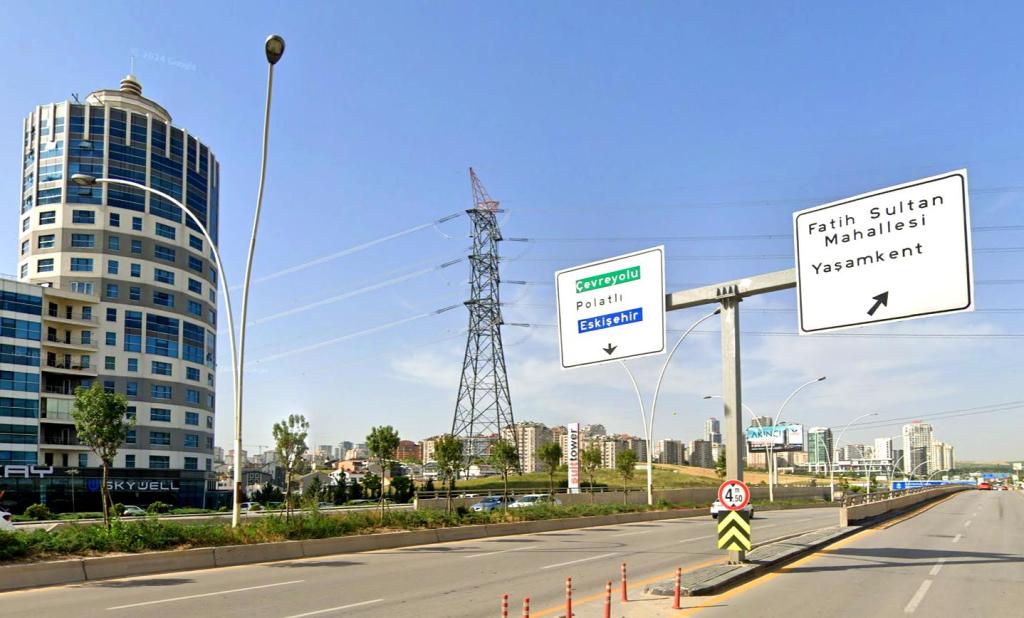 Eskişehir Yolu üzerinde Yaşamkent ve Fatih Sultan Mahallesi yönlendirme tabelaları ve konut silueti
